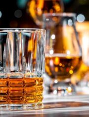 American bourbon whiskey in glass with bottles of strong drinks on dark green background